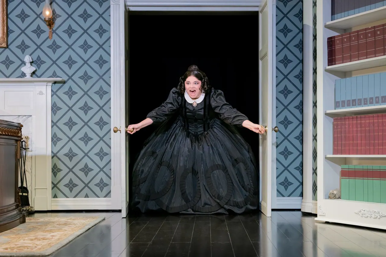 A performer in a black dress standing in a doorway in Oh, Mary!